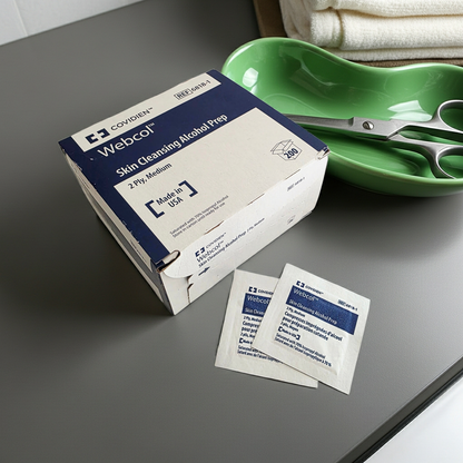 Box of Webcol Skin Cleansing Alcohol Prep packets on a gray surface with a green kidney dish and scissors.