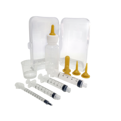 A bottle and syringe feeding kit for neonates, including a clear plastic bottle, multiple feeding teats, luer lock syringes in different sizes, a measuring cup, and a clear plastic storage case.