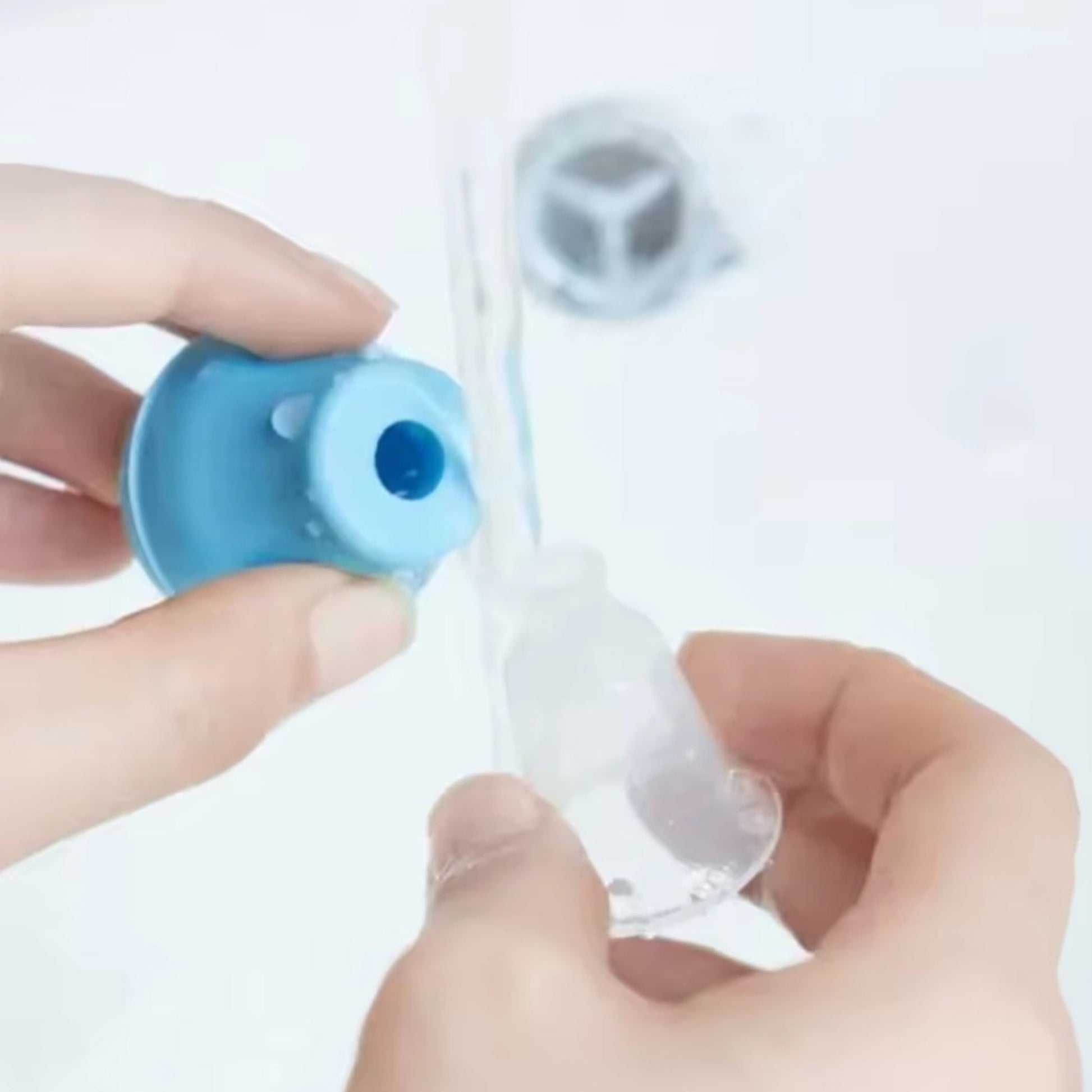Person holding and cleaning a blue inverted nipple corrector  against a white background