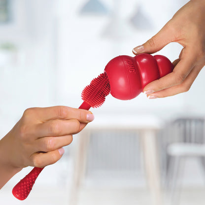 Red KONG Cleaning Brush being held by two hands against a blurred background
