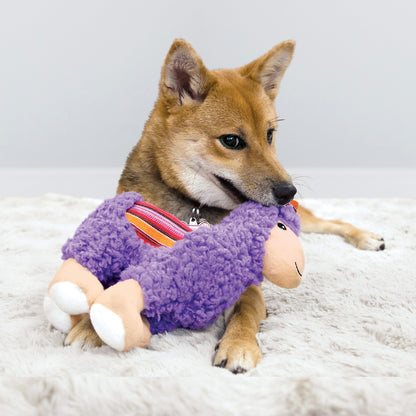 Dog playing with a purple KONG Sherps Llama plush toy on a light gray surface