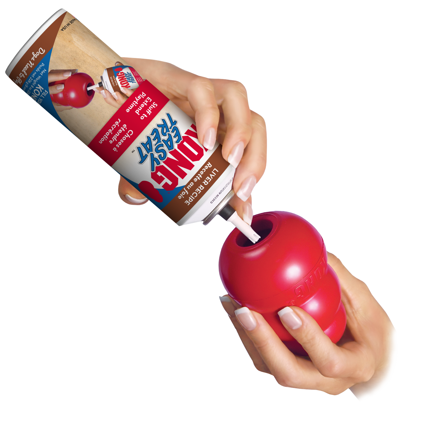 A hand holding a red KONG Easy Treat Paste container with a nozzle, dispensing the treat paste onto a Kong Classic red KONG toy.