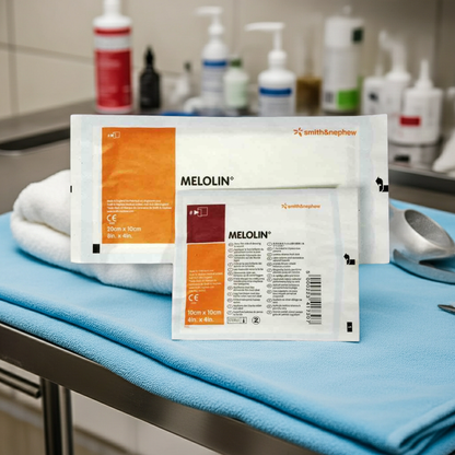 Two packages of Melolin bandages on a blue surface with medical equipment in the background.