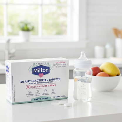 Milton anti-bacterial tablets box on a kitchen counter with a baby bottle and fruit.