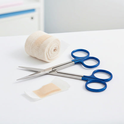 Pair of scissors with blue handles on a white surface, next to a roll of bandage and a bandage.