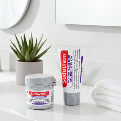 Sudocrem jar and tube on a bathroom counter with a plant and towel in the background