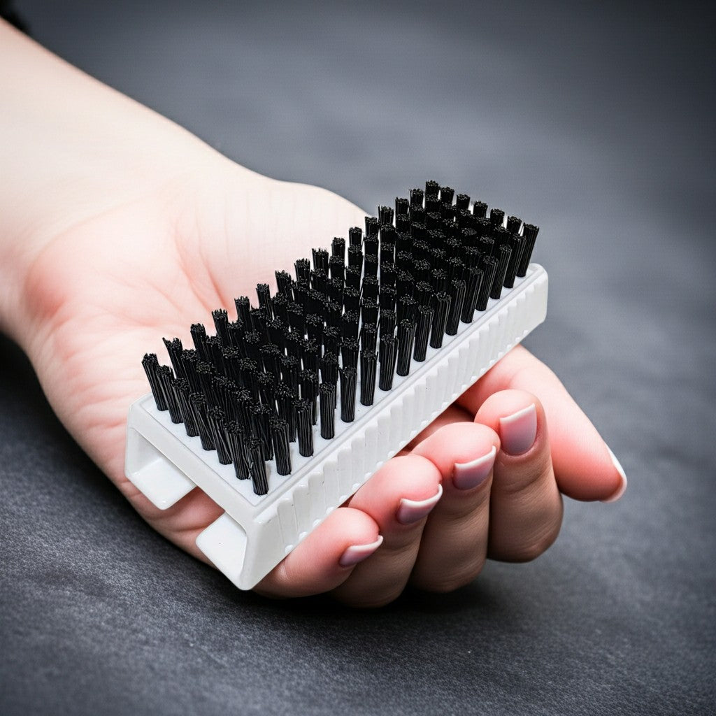 Hand holding a white surgical scrub brush with black bristles on a dark background