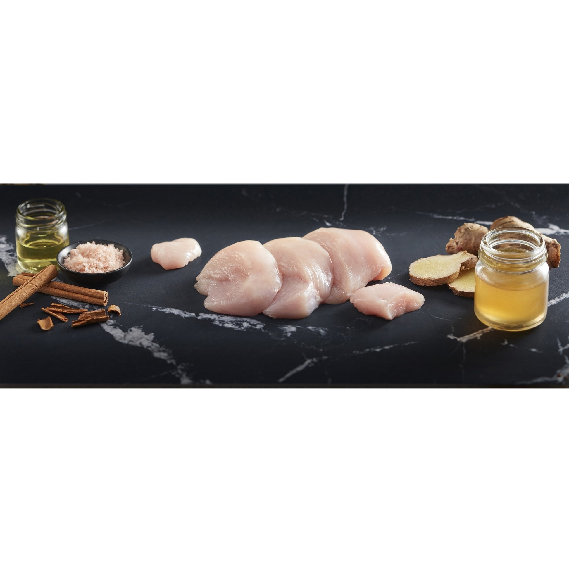 Black Hawk Ingredients of Raw chicken pieces on a black marble surface with spices and herbs.